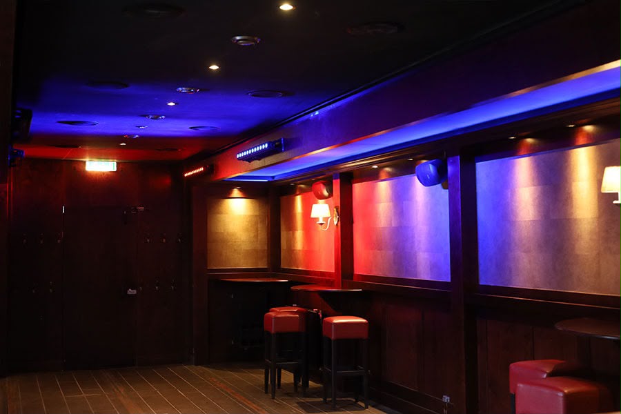 Het interieur van De Kroeg XL met houten lambrisering, barkrukken en blauw-rode sfeerverlichting.
